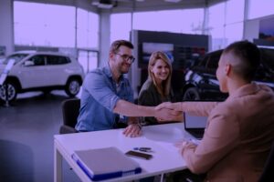 Male customer and female car dealer shaking hands at showroom.