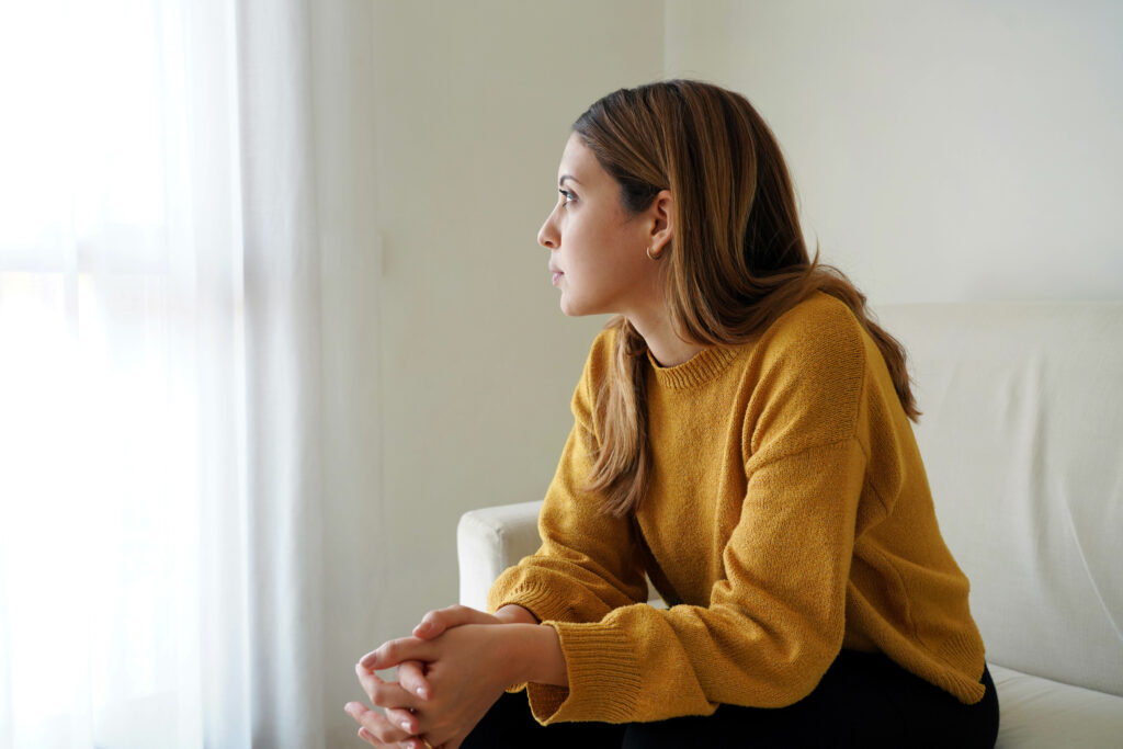 Melancholic sad woman looking through the window at home