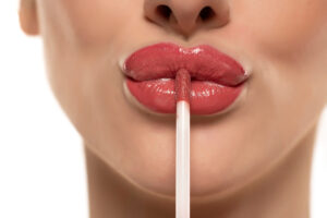 young beautiful woman apply a lip gloss on her lips on white background.