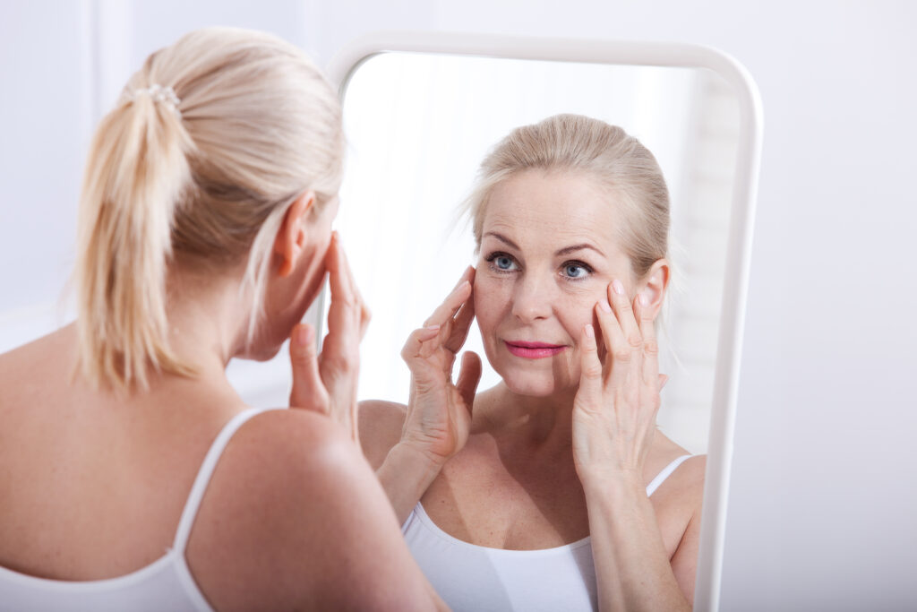 Middle aged woman looking at wrinkles in mirror. Plastic surgery and collagen injections. Makeup. Macro face. Selective focus on the face. Realistic images with their own imperfections.